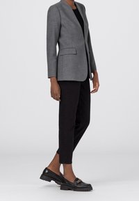 Šedé sako na míru s klopovým límcem, jednobutonovým zapínáním a dvěma předními kapsami, doplněné černými krátkými kalhotami a černými mokasíny.