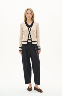 Cardigan beige en tricot avec des accents noirs, col en V et boutons dorés, associé à un pantalon noir ample et des ballerines à imprimé léopard.