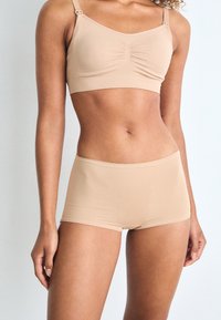 Beige seamless bralette with adjustable straps and gathered detail, paired with matching high-waist shorts made of soft, stretchy fabric.