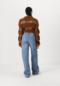 Rjav puhast pleten džemper z odprtimi mrežnimi detajli, v kombinaciji z svetloblue širokimi jeans hlačami. Džemper ima vzorčaste črte; jeans imajo sproščen kroj.