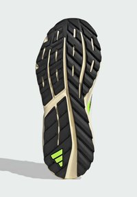 Czarna gumowa podeszwa buta z głębokim bieżnikiem, z beżową środkową częścią oraz zielonym odblaskowym akcentem na pięcie. Teksturowana dla lepszej przyczepności.