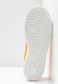 Semelle de sneaker Nike affichée, présentant un dessus orange vif et une semelle extérieure en caoutchouc blanc texturé avec des motifs circulaires et des détails de logo.