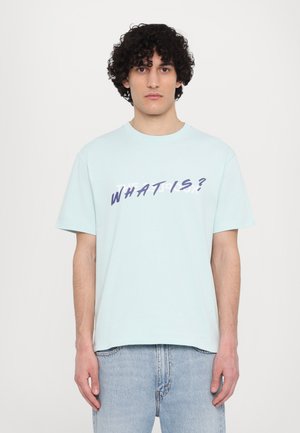 T-shirt en coton bleu clair avec des manches courtes et un col rond, présentant un texte en gras "QU'EST-CE QUE C'EST ?" dans une couleur foncée contrastante sur le devant.