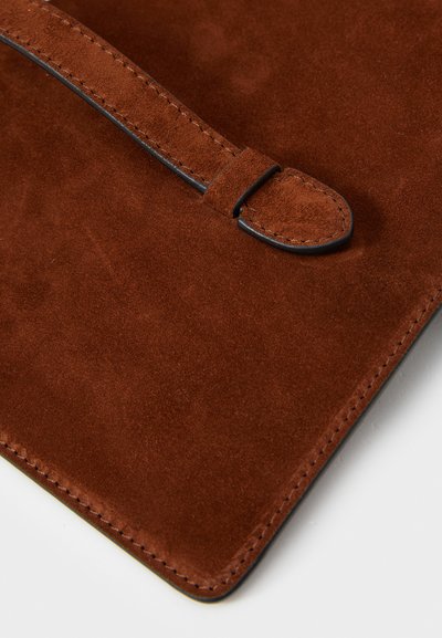 Material din suede maro, textură netedă, design minimalist, cu margine cusută și detaliu de închidere cu o curea subțire neagră.