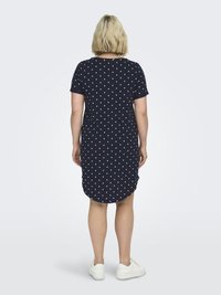 Vestido azul marino oscuro con mangas cortas, decorado con lunares blancos, un dobladillo redondeado y un corte relajado. Combinado con zapatillas blancas.