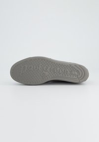 Semelle de chaussure en caoutchouc gris avec un motif de grip circulaire ; présente un nom de marque et un logo en relief ; texture lisse avec une légère courbure.
