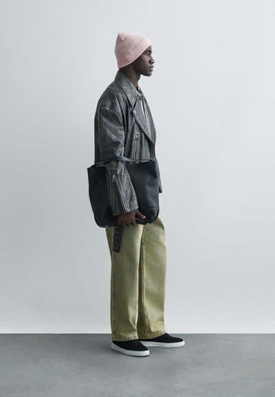 Zwarte leren schoudertas, grijze leren jas, patroonhemd, gele wijd uitlopende jeans, roze gebreide beanie en zwarte sneakers.