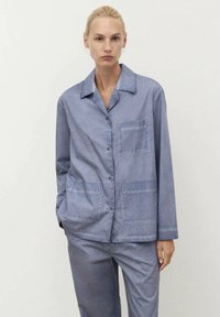 Camicia azzurra chiara con colletto, realizzata in tessuto morbido, presenta una chiusura con bottoni e due tasche a toppa sul davanti. Vestibilità rilassata.