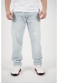 Jeans de mezclilla azul claro con un corte relajado, piernas rectas y un leve desvanecimiento. Combinados con zapatillas blancas con acentos rojos.