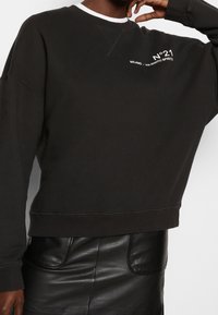 Sudadera negra con ribete blanco en el cuello; presenta el texto "MILANO" y "No.21" en blanco. Hecha de un tejido suave; ajuste relajado.