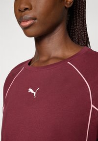 Burgunderfarget sweatshirt med rosa detaljer og en hvit Puma-logo på brystet. Har rund hals og raglan-sømdesign.
