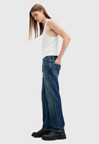 Jeans holgados de color azul oscuro con cinco bolsillos, confeccionados en denim. Combinados con una camiseta sin mangas ajustada blanca y botas negras gruesas.