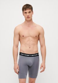 Sive sportske bokserice s crnim pojasom na kojem se nalazi logo "Jordan Sport". Uzani kroj, glatka tkanina i dužina do sredine bedra.