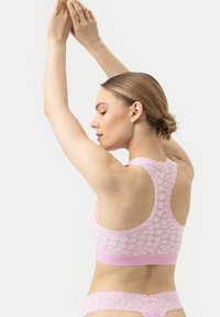 Bralette en dentelle rose avec un design dos nu, présentant une superposition de dentelle texturée et une bande élastique lisse en bas.