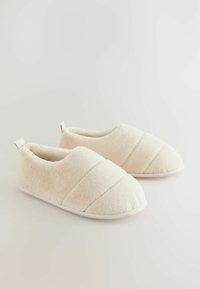 Beige fleece slippers met een ronde neus, voorzien van gequiltte accenten en een trekband aan de achterkant. Zachte textuur en een gevoerde zool.