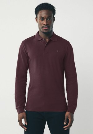 Polo à manches longues bordeaux avec col et poignets côtelés. Présente un logo discret sur la poitrine. Tissu doux et lisse.