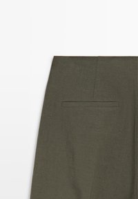 Mørkegrønt stof nederdel sektion med en enkelt vandret kantlomme og synlige sømdetaljer på en hvid baggrund.