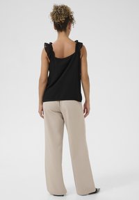 Top negru fără mâneci, cu bretele volanate, asortat cu pantaloni largi bej. Textură de țesătură netedă, design simplu, privire din spate.