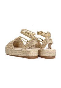 Sandalias de plataforma de paja tejida con tiras cruzadas, color beige, superficie texturizada y suela marrón sólida, con detalles de cuerda.