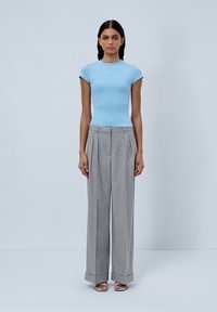 Light blue fitted t-shirt with short sleeves, paired with high-waisted, gray pleated trousers; model wearing silver sandals.