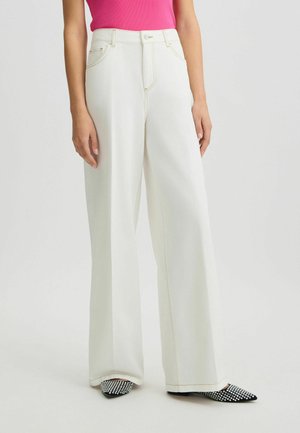 Pantalons blancs à jambe large avec des coutures contrastées, poches avant et taille haute. Associés à des chaussures pointues texturées noires et blanches.