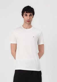 Tricou alb din bumbac, cu mâneci scurte, guler rotund și un logo mic, roșu, alb și albastru pe piept. Textură netedă, formă ajustată.
