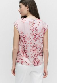 Ärmlös rosa blus med blommönster i olika nyanser av rosa. Har en liten öppning bak med en knappstängning. Mjuk tyg.