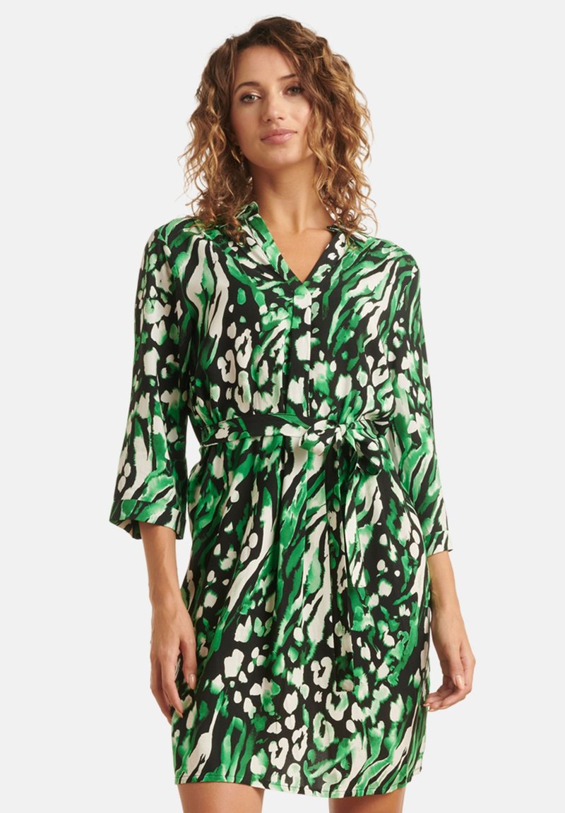 Grün und schwarz gemustertes Kleid mit V-Ausschnitt, Dreiviertelärmeln und einer Taillierung. Hergestellt aus glattem Stoff mit einem auffälligen Design.