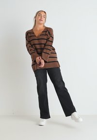 Pull surdimensionné à rayures marron avec un décolleté en V profond, associé à un pantalon large noir et des baskets blanches. Texture de tissu lisse.