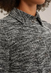 Camicia in tessuto testurizzato bianco e nero con colletto, dotata di piccoli bottoni neri e un motivo intrecciato. Morbido al tatto e design strutturato.