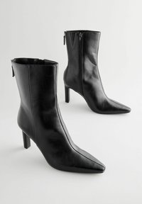 Stivaletti neri in pelle con punta affusolata e chiusura con zip. Presentano un design elegante e un tacco a stiletto di media altezza.