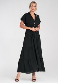 Czarna maxi sukienka z krótkimi rękawami, zapinana na guziki z przodu, o warstwowej konstrukcji. Wykonana z lekkiego materiału, posiada wiązany pas w talii oraz swobodny krój.