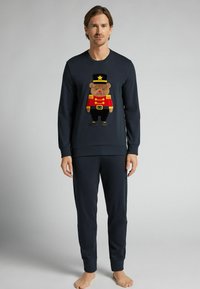 Námořnická modrá mikina s vyšitým medvídkem v červené uniformě a černém klobouku. Vzorované s odpovídajícími námořnickými modrými tepláky.