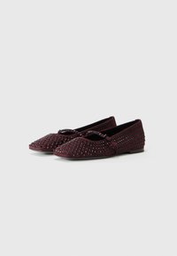 Chaussures plates bordeaux en suède, ornées de clous métalliques. Elles ont un bout pointu et une petite bride à la cheville pour un maintien sécurisé.