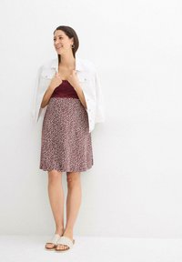 Robe bordeaux avec un motif abstrait blanc et rose clair, assortie d'une veste en denim blanche et de chaussures slip-on en toile beige.