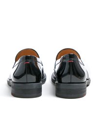 Schwarze Lacklederschuhe mit einer runden Zehenform und niedrigem Absatz, die eine glatte Textur und dezente rote Stichdetails am Absatz aufweisen.