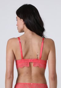 Reggiseno con schienale in pizzo color corallo, dotato di spalline in satin regolabili, chiusura con gancio e occhiello e dettagli in pizzo intricati lungo la fascia.