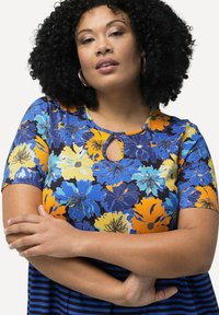 Top con estampado floral y mangas cortas, que presenta flores azules, amarillas y naranjas sobre un fondo oscuro. Escote tipo ojo de cerradura y dobladillo a rayas.