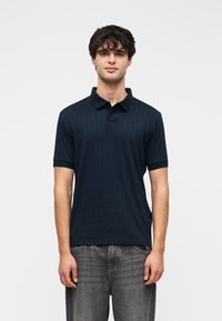 Polo bleu marine à manches courtes avec une texture côtelée subtile et un col classique, associé à un jean en denim gris clair.