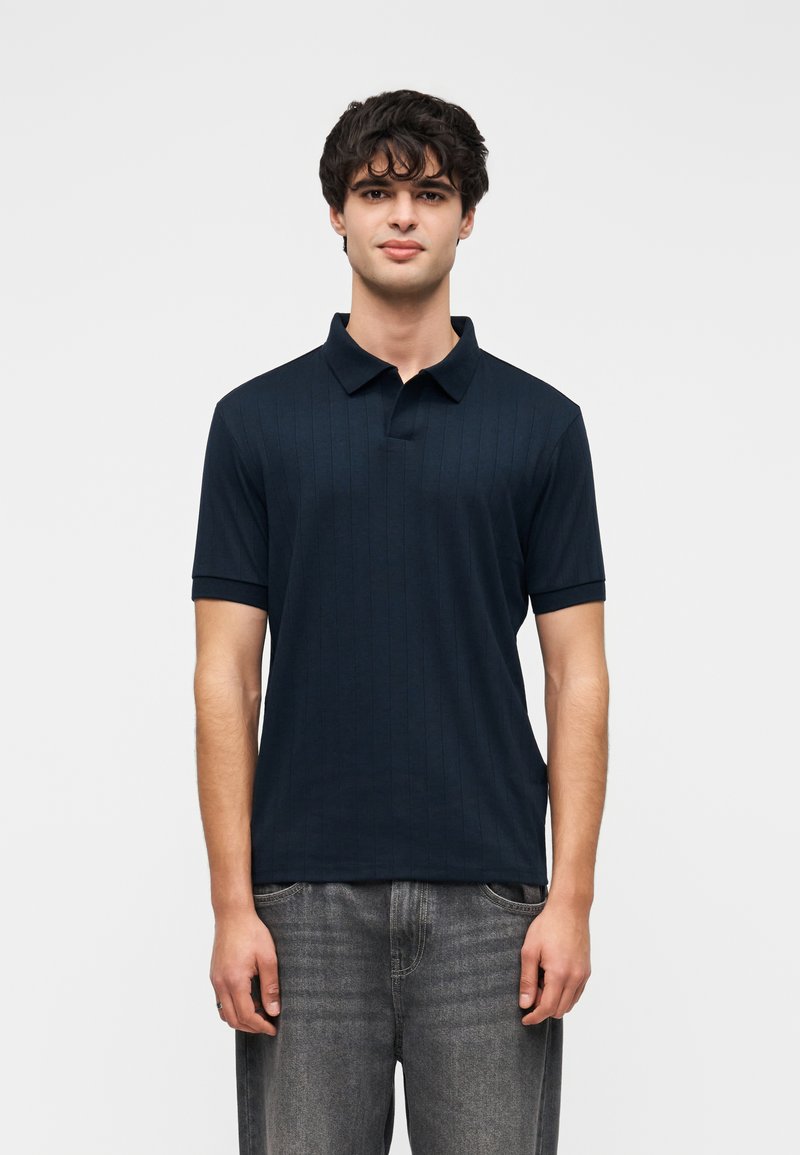 Polo bleu marine à manches courtes avec une texture côtelée subtile et un col classique, associé à un jean en denim gris clair.