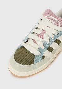 Baskets multicolores avec une tige texturée verte, bleue et rose, des lacets blancs et une semelle en caoutchouc naturel avec trois rayures sur le côté.