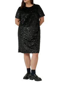 Czarna sukienka z cekinami, z krótkimi rękawami, o zaokrąglonym dekolcie i prostym kroju. Noszona z czarnymi masywnymi butami i granatowymi skarpetkami.