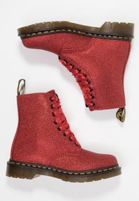 Röda glittrande ankelstövlar med glänsande snören, rund tå och svart gummisula. Har en dragflik bak och gula sömnadsdetaljer.