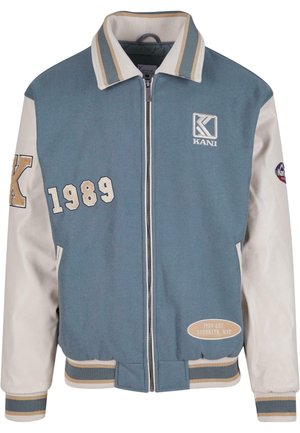 Jachetă varsity albastră și crem cu fermoar frontal, guler și manșete ribbate. Prezintă logo-ul „KANI”, brodat 1989 și detalii din Brooklyn, NYC.