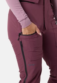 Bordeaux isolerede bukser med en tætsiddende pasform, lynlås-lommer og RECCO® branding. Stoffet er glat og en smule strækbart.
