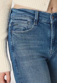 Světle modré denimové džíny s vybledlým povrchem, designem s pěti kapsami, zapínáním na knoflík vpředu a diskrétním logem značky na přední kapse.