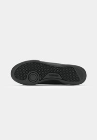 Semelle de sneaker noire en caoutchouc texturé, dotée d'un logo circulaire et d'un motif de carrés et de lignes pour une meilleure adhérence. Bords lisses et forme arrondie.