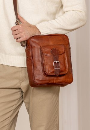 Brun læder crossbody taske med klap, justerbar rem og metalspænde. Glat tekstur med synlige syninger og en frontlomme.