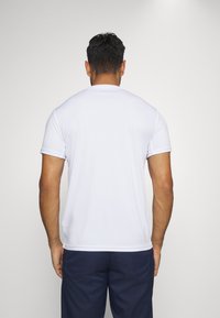 Witte sportieve T-shirt met korte mouwen, een gladde textuur, een eenvoudig ontwerp, ronde halslijn en minimale stikdetails, gedragen met marineblauwe shorts.