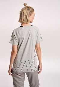 Grå kortärmad t-shirt med rundad fåll, som har svarta geometriska mönster på baksidan och en kontrasterande halsringning. Justerbar passform.